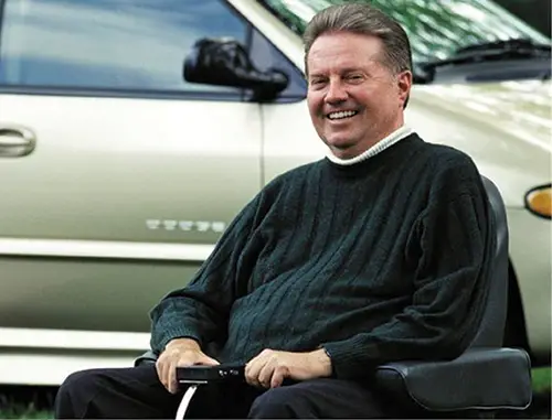 https://www.inclusionproject.org/inclusionpioneer2/ Ralph Braun in a wheelchair wearing a black jumper with short brown hair in front of a car