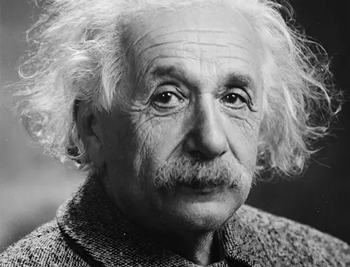 A black and white image of Albert Einstein with frizzy white hair and a moustache wearing a thick wool jacket
